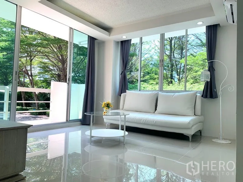 Condominium for rent or sale in Khlong Toei, Bangkok - Corner living area with white sofa, round glass coffee table and floor-to-ceiling windows to trees.