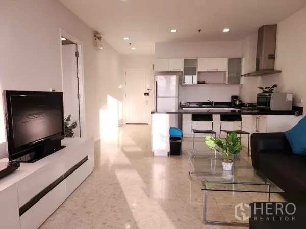 Condominium for rent in Khlong Toei, Bangkok - Open-plan living room and kitchen with white cabinetry, island counter and TV console.
