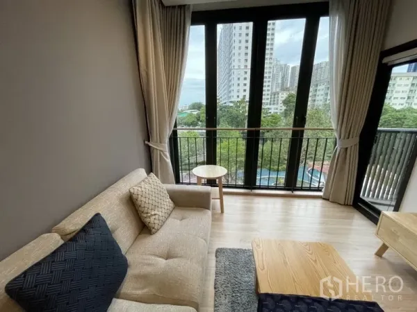 公寓 出租在Watthana, Bangkok - 明亮客厅，落地窗与阳台栏杆，眺望城市与绿意。