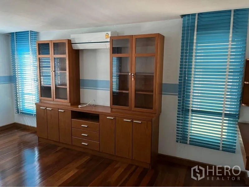 Townhouse for sale in Phra Khanong, Bangkok - Bedroom with built-in glass-door cabinet, blue blinds, air-conditioning, and wood floors.