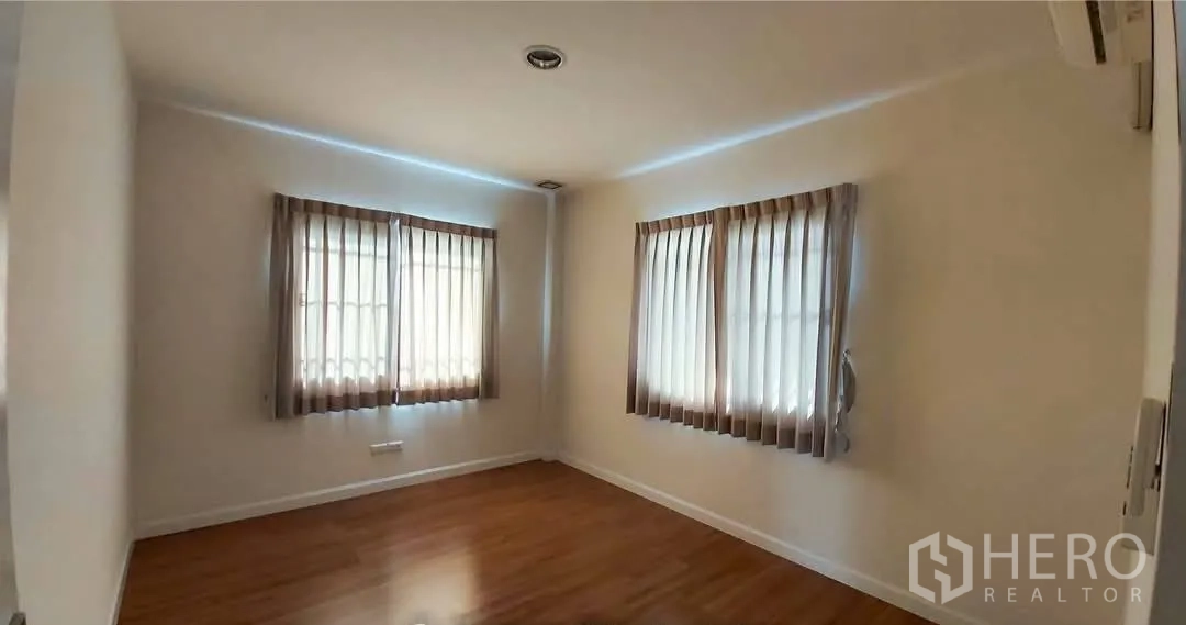 Detached House for sale in Bang Kapi, Bangkok - Bright secondary bedroom with two corner windows, curtains and wood floors.