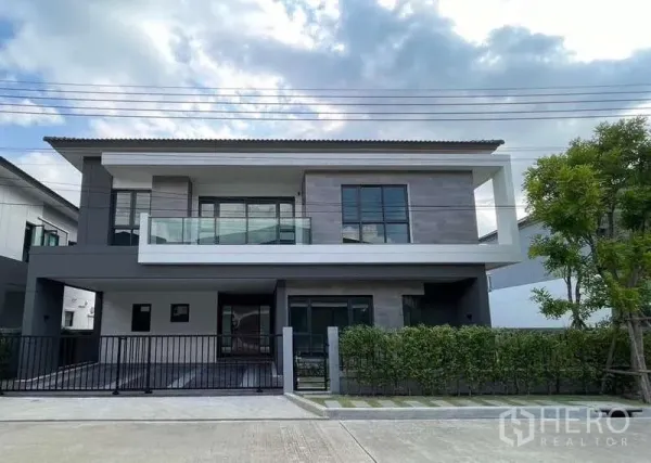 独立式住宅 出租在Bang Phli, Samut Prakan - 现代两层独栋别墅正立面，玻璃阳台和车道大门