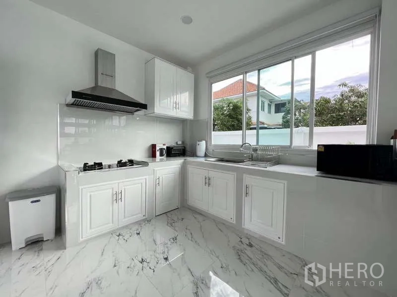 Detached House for rent in Lat Krabang, Bangkok - Bright white kitchen with gas hob, range hood and marble floors by a large window.