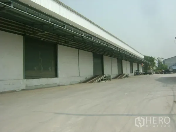 货栈 出租在Mueang Samut Sakhon, Samut Sakhon - 仓库长立面，多个装卸平台，前方宽阔车道可容拖车。