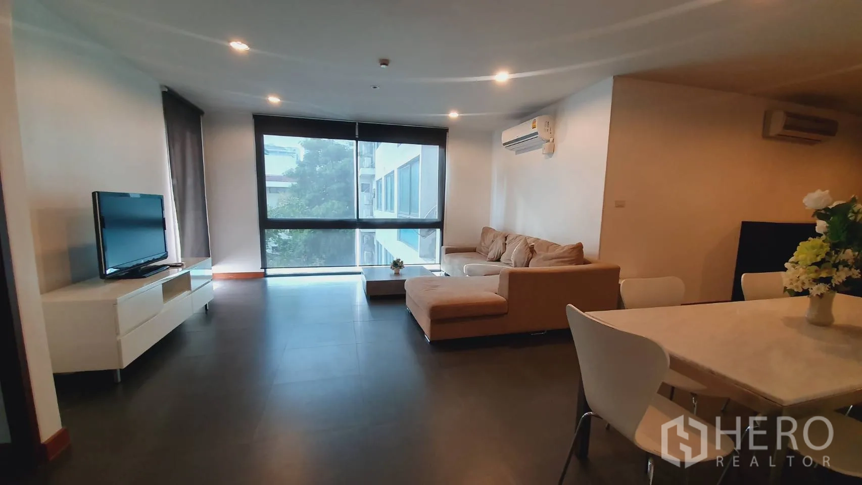 公寓 出租在Khlong Toei, Bangkok - 明亮客厅，大幅窗户、遮光卷帘与电视柜。