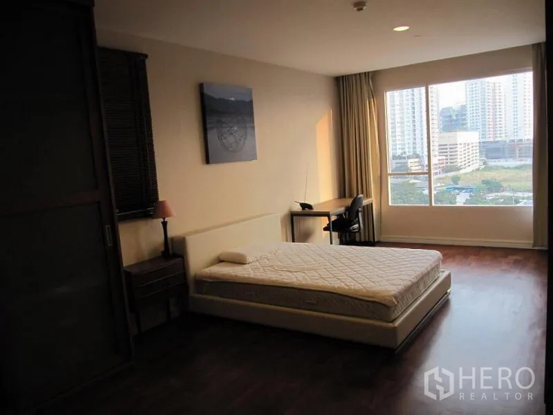 Condominium for rent in Khlong Toei, Bangkok - Large bedroom with platform bed, study desk by a wide window, and city view.