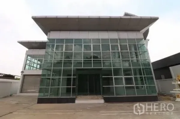 Warehouse for rent or sale in Prawet, Bangkok - Front elevation of the modern glass curtain wall building with a wide driveway.