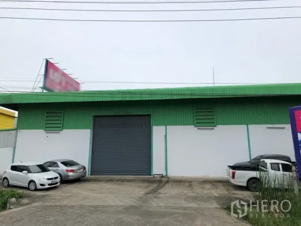 Factory for rent in Pathum Thani - Warehouse facade with green cladding, large roller shutter and on-site parking area.