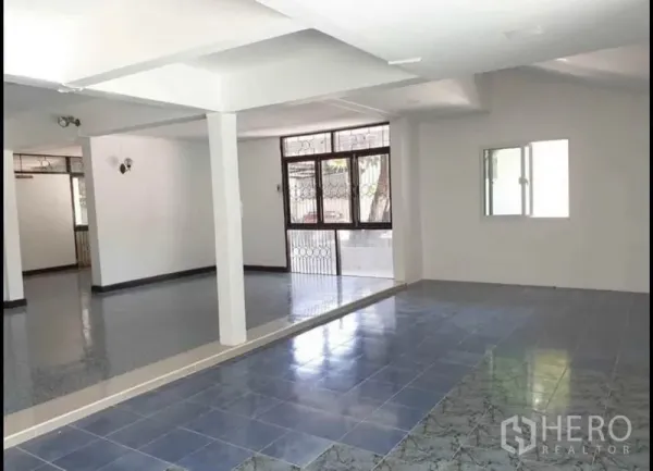 独立式住宅 出租在Lat Phrao, Bangkok - 一层开放式空间，混合瓷砖地面、白色立柱与带防盗格栅的窗户。