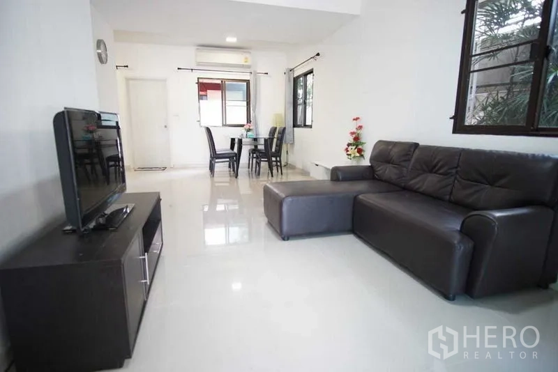 Townhouse for rent in Suan Luang, Bangkok - Spacious living room with L-shaped leather sofa and TV console facing windows.