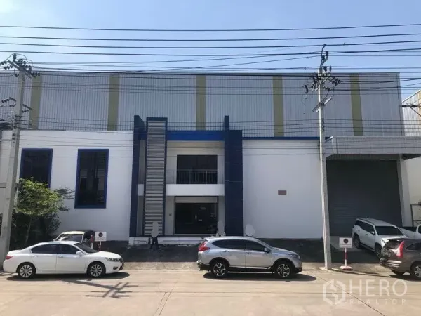 Factory for rent or sale in Samut Prakan - Modern factory exterior in Bang Phli with office entrance, parking and a loading bay with roller shutter.