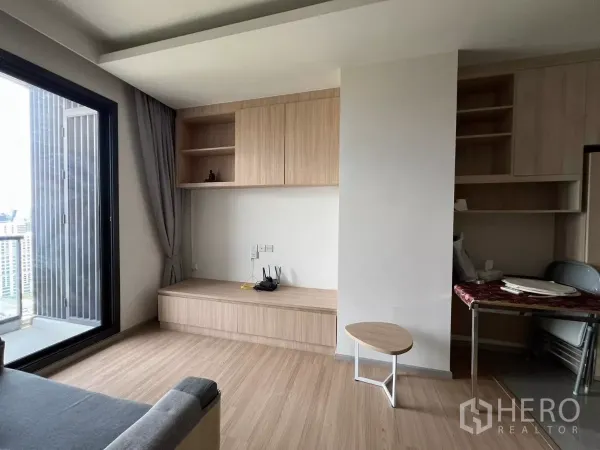 Condominium for rent or sale in Chatuchak, Bangkok - Bright living area with light‑wood built‑in cabinets and a balcony showcasing a city view in a Chatuchak condo.