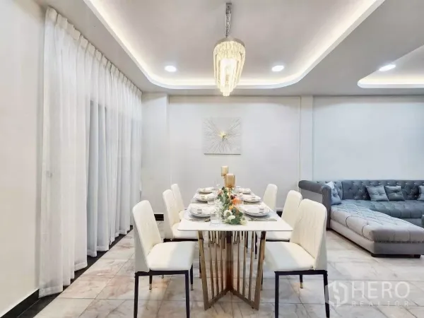 Townhouse for rent in Huai Khwang, Bangkok - Six-seat dining table with white chairs beneath a crystal pendant next to long drapes.
