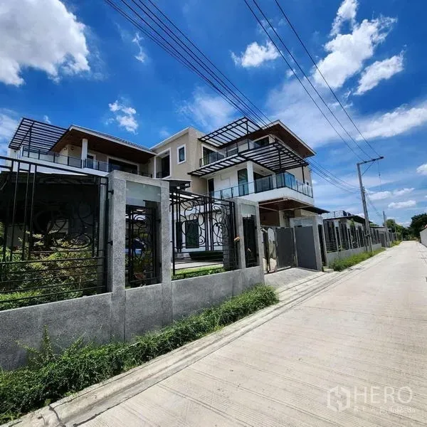 独立式住宅 出售在Phra Khanong, Bangkok - 三层现代独栋别墅外观，玻璃阳台与混凝土围墙，静谧街景
