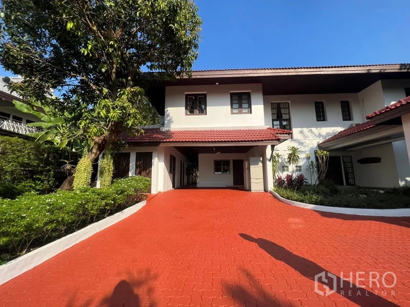 Detached House for rent in Bang Phli, Samut Prakan - Front facade with covered carport, red brick driveway, and mature greenery around the two-storey home.