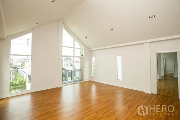 Detached House for rent or sale in Lam Luk Ka, Pathum Thani - Bright double-height living area with floor-to-ceiling windows and warm wood floors.