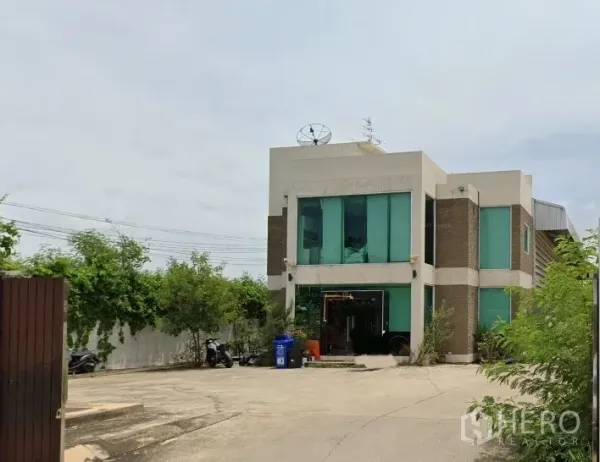 Factory for rent in Bang Bua Thong, Nonthaburi - Two-storey factory office building in Bang Bua Thong, Nonthaburi with green-tinted windows, wide concrete yard and gated entrance.
