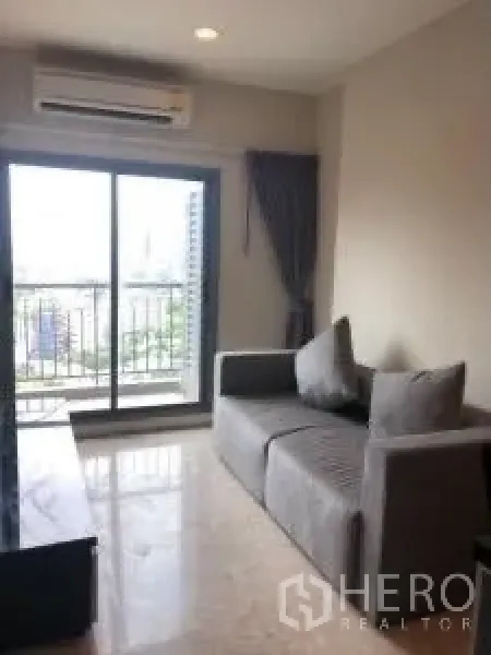 Condominium for rent or sale in Khlong Toei, Bangkok - Bright living room with gray sofa, marble floor and balcony overlooking the city.