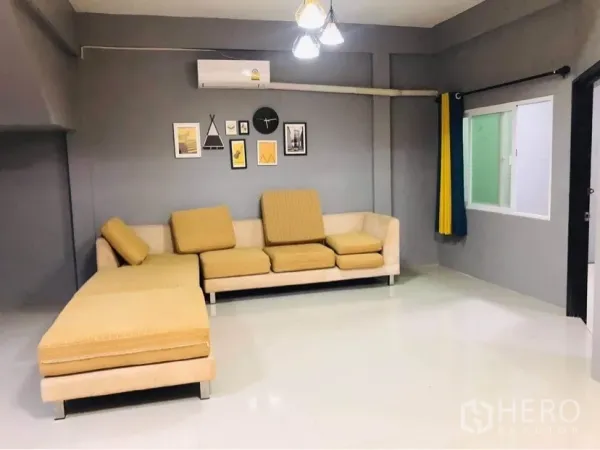 联排别墅 出租或出售在Huai Khwang, Bangkok - 宽敞客厅，L形沙发、灰色墙面、空调与墙面装饰画。