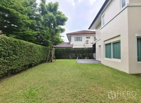 Detached House for rent or sale in Lat Krabang, Bangkok - Wide grassy yard along the house with hedges, a tree and a small tiled terrace.