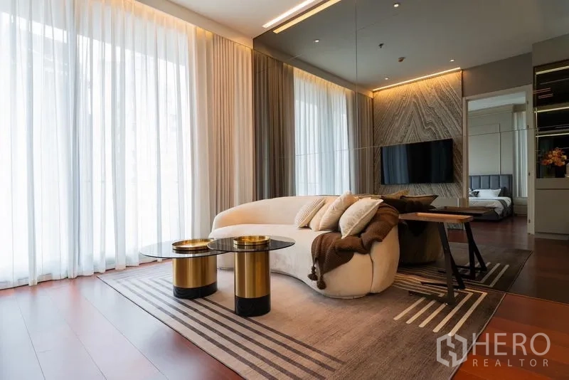 Condominium for rent in Watthana, Bangkok - Living room with curved sofa, gold coffee tables, large rug and floor‑to‑ceiling drapes.