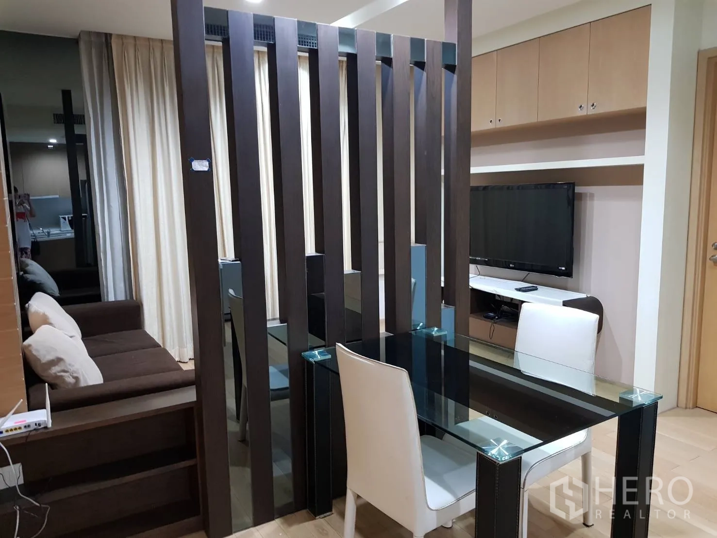 Condominium for rent in Khlong Toei, Bangkok - Open-plan living area with a glass dining table, wood room divider, sofa and TV cabinet.