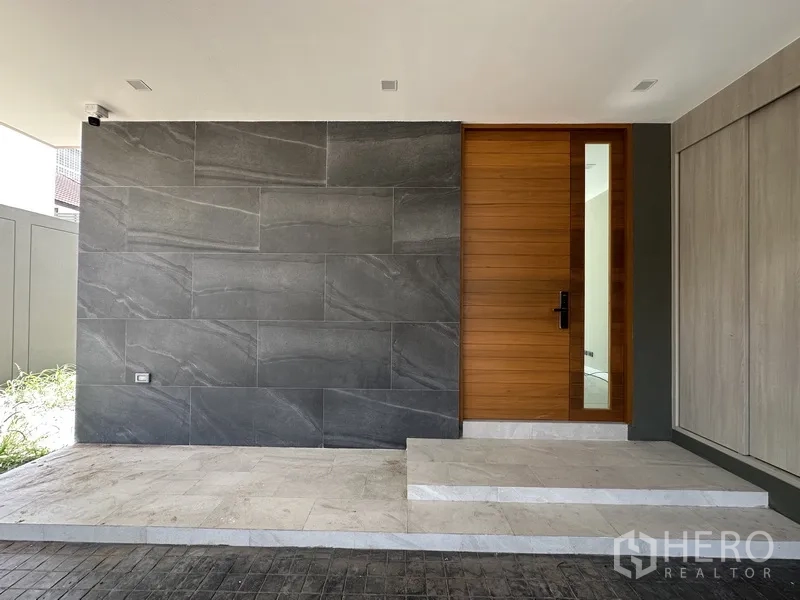 家庭办公室 for rent or sale in Suan Luang, Bangkok - 入口处深色石材特色墙与木质前门，带遮棚。