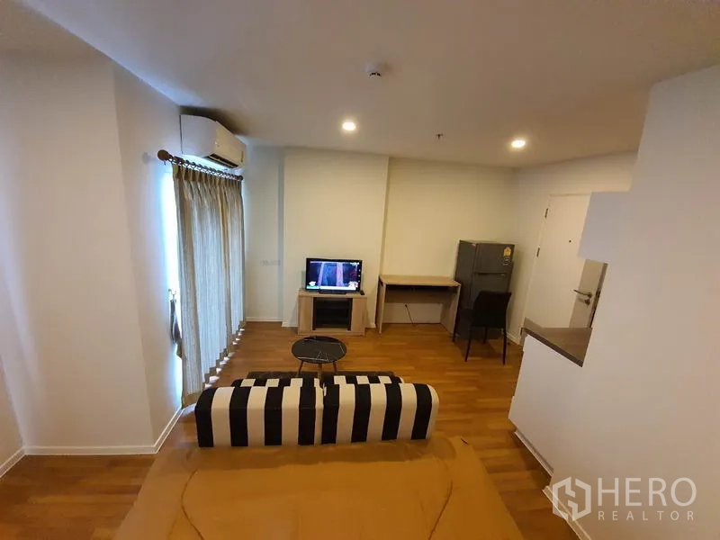 公寓 出售在Chatuchak, Bangkok - 乍都节公寓客厅，条纹沙发、电视、书桌与冰箱，木地板温馨明亮。