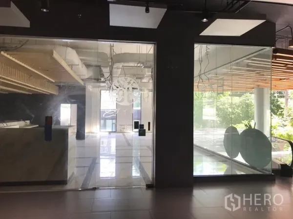 Retail Space for rent in Khlong Toei, Bangkok - Glass storefront with sliding doors and floor-to-ceiling windows, overlooking greenery with a nearby escalator.