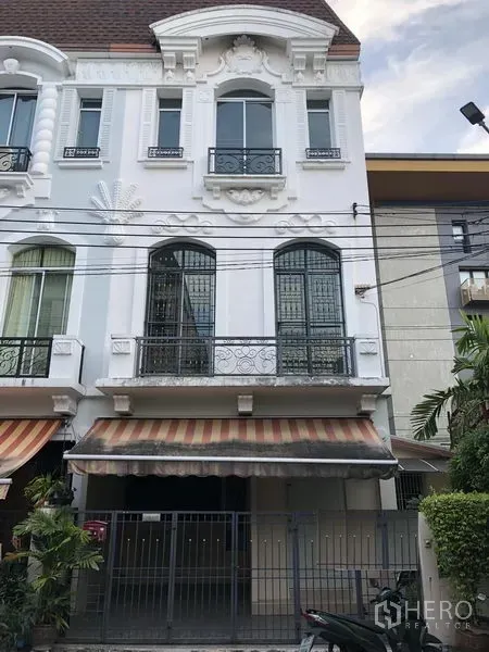 Townhouse for rent in Wang Thonglang, Bangkok - Three-storey European-style townhouse facade with wrought-iron balconies, striped awnings and a gated carport in Wang Thonglang, Bangkok.