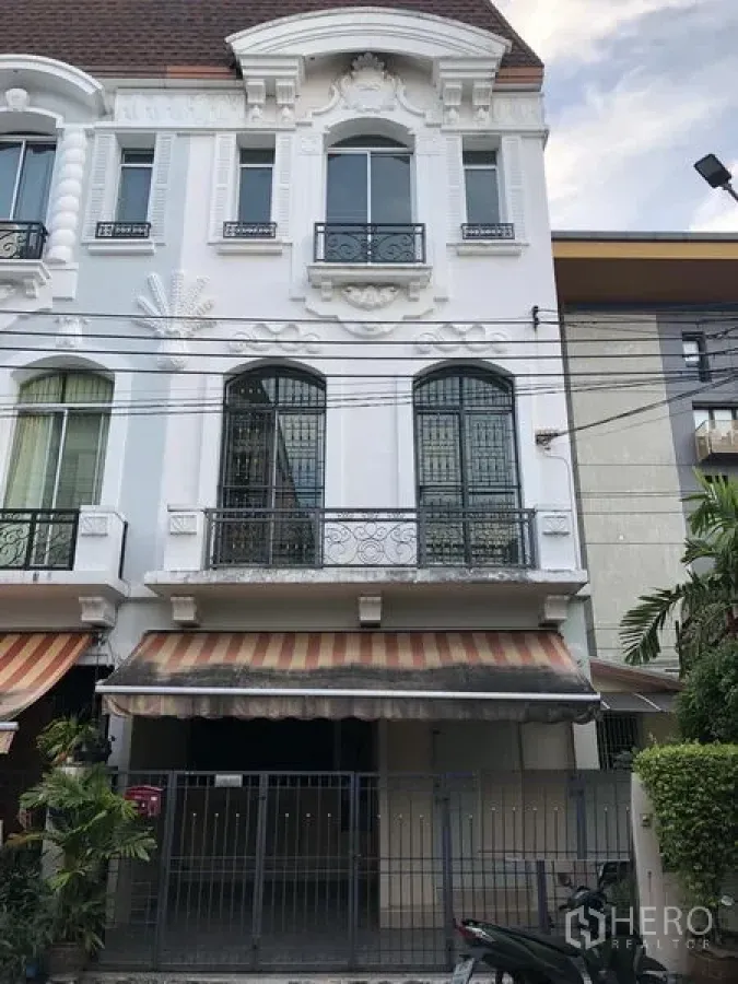 联排别墅 出租在Wang Thonglang, Bangkok - 三层欧式联排别墅外立面，铁艺阳台、条纹雨棚与带围栏车位，位于曼谷Wang Thonglang。