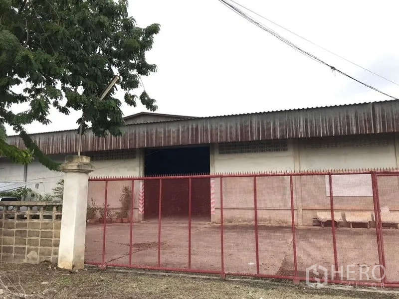 Warehouse for rent in Mueang Nakhon Pathom, Nakhon Pathom - Street‑facing facade with red perimeter fence and main entrance gate.