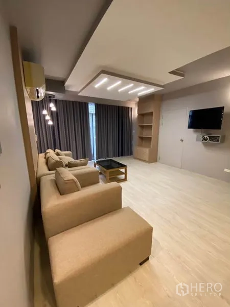 คอนโด ให้เช่าในWatthana, Bangkok - ห้องนั่งเล่นกว้าง โซฟาสีเบจ ผนังทีวี ชั้นบิวท์อิน ไฟดาวน์ไลท์และผ้าม่านทึบแสง