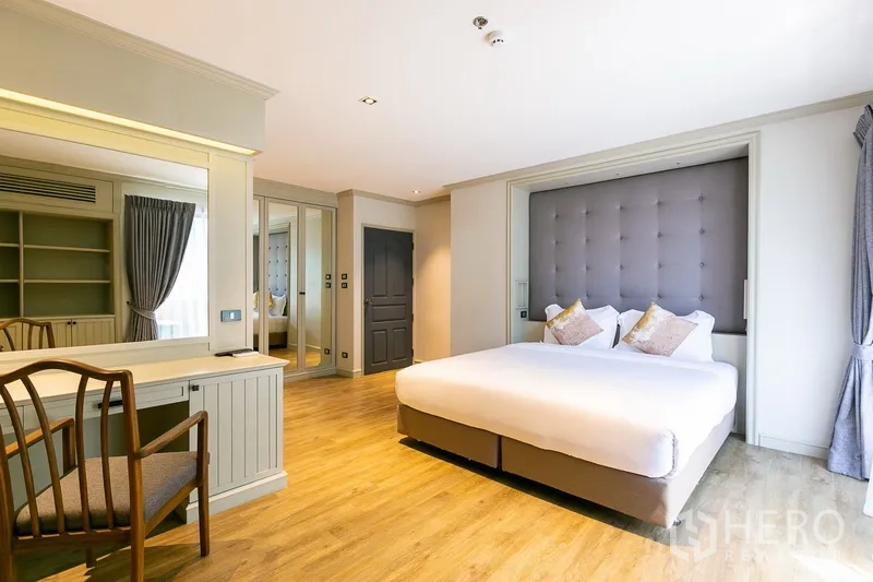 Apartment for rent in Khlong Toei, Bangkok - Second bedroom with padded headboard wall, vanity desk and large windows.