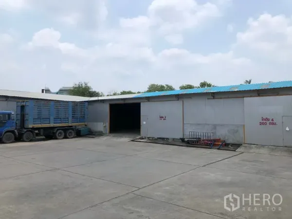 Warehouse for rent in Mueang Pathum Thani, Pathum Thani - Warehouse exterior with multiple loading bays and a parked container truck on a spacious driveway.