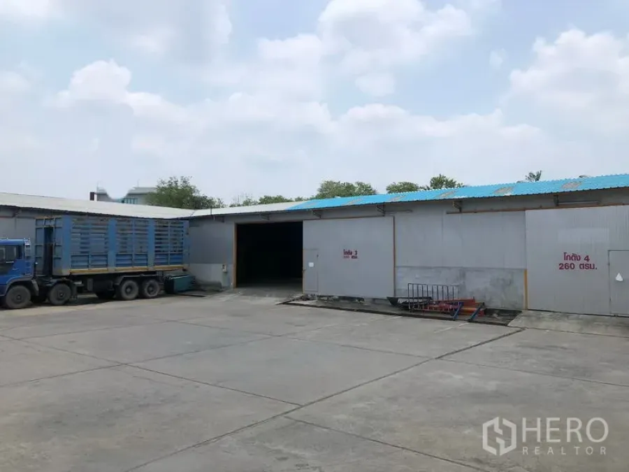 Warehouse for rent in Mueang Pathum Thani, Pathum Thani - Warehouse exterior with multiple loading bays and a parked container truck on a spacious driveway.