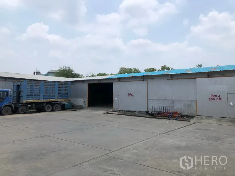 Warehouse for rent in Mueang Pathum Thani, Pathum Thani - Warehouse exterior with multiple loading bays and a parked container truck on a spacious driveway.