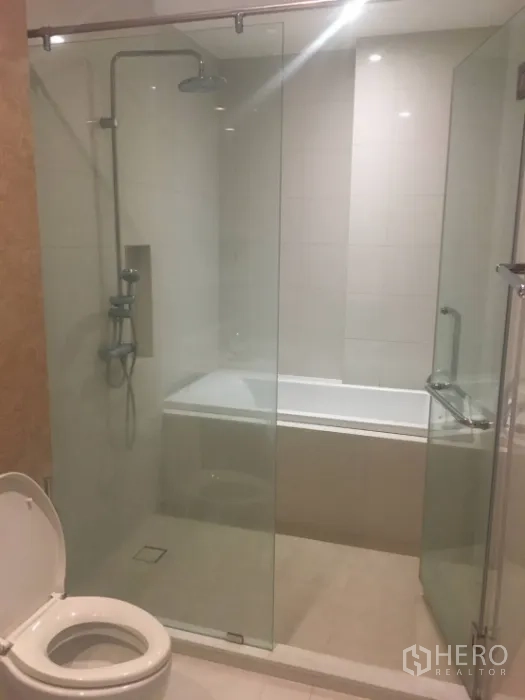 Condominium for rent in Khlong Toei, Bangkok - Bathroom with glass-enclosed shower, bathtub and clean white tile finishes.