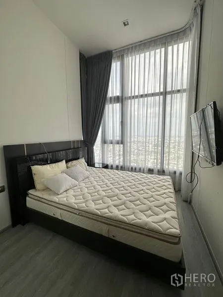 Condominium for rent in Phra Khanong, Bangkok - Primary bedroom with a large bed, wall-mounted TV and curtain-lined corner windows with city view.