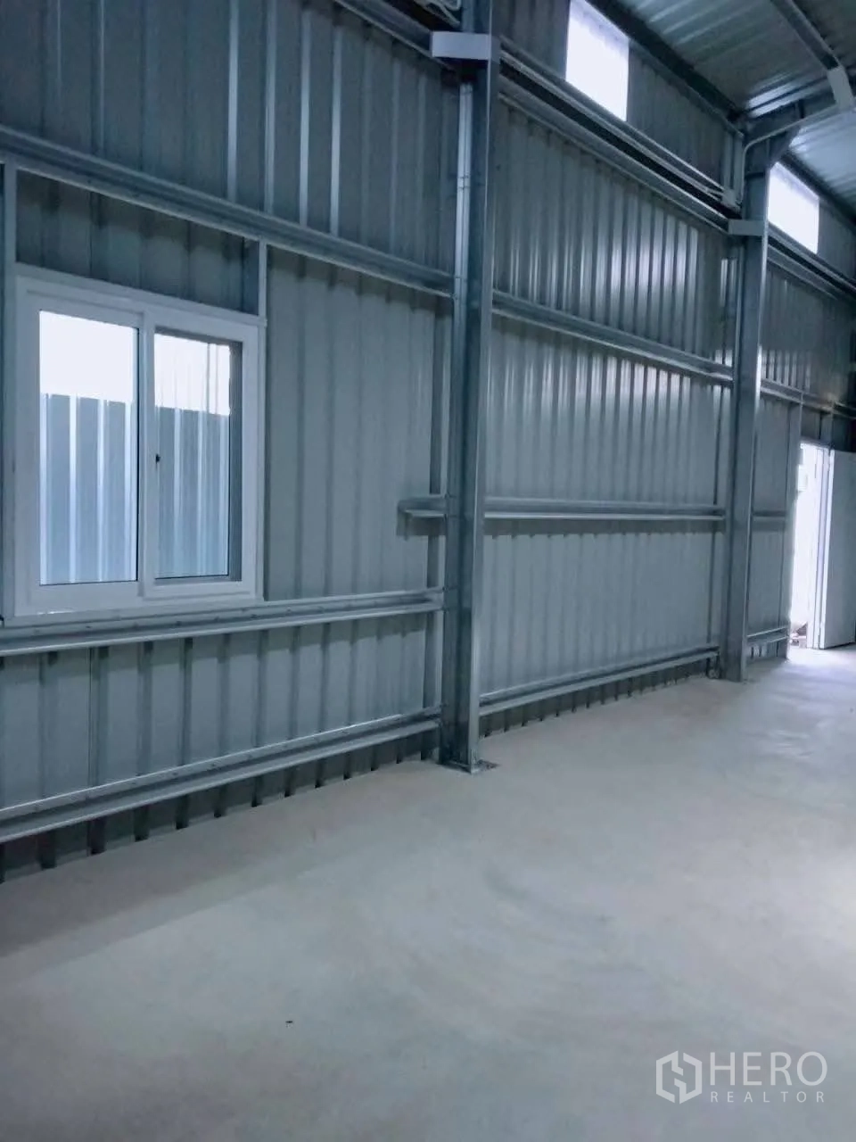 Warehouse for rent in Lat Phrao, Bangkok - Warehouse wall detail showing steel structure, high windows, and smooth concrete floor.