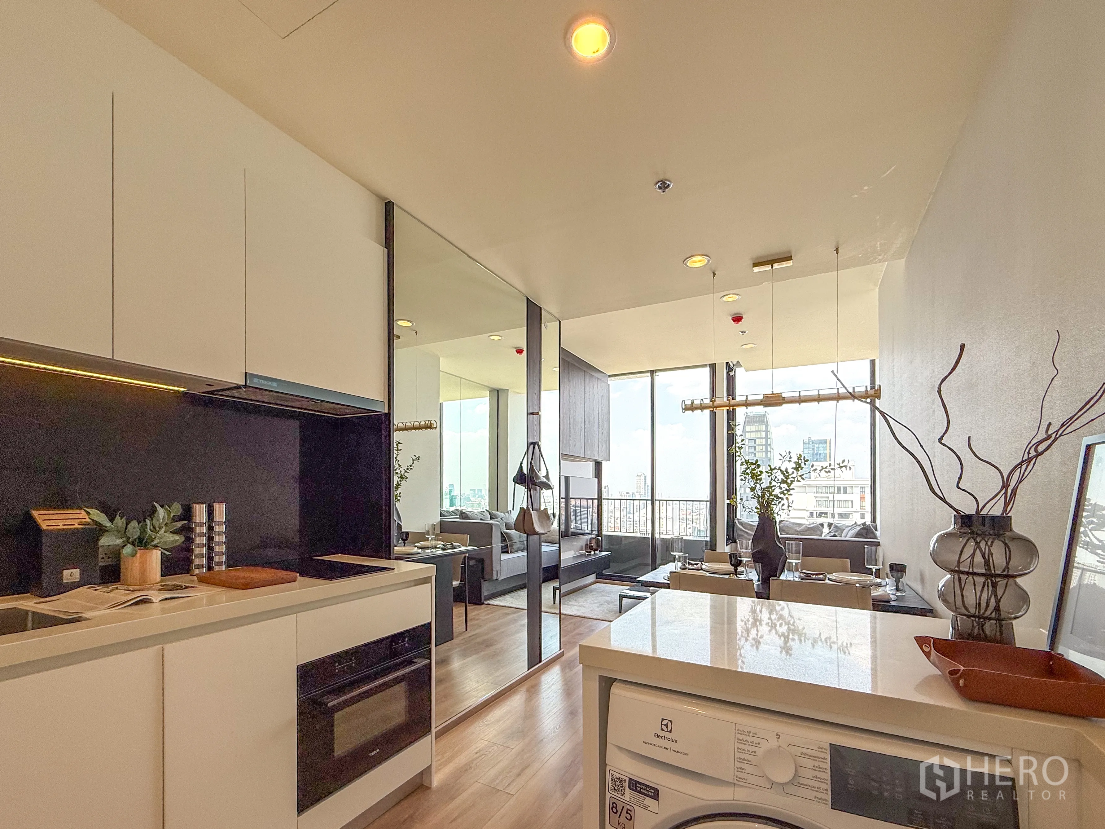公寓 for sale in Watthana, Bangkok - 开放式厨房配备嵌入式炉灶与烤箱及洗衣机，连接明亮的餐客区，落地窗享城市景观。