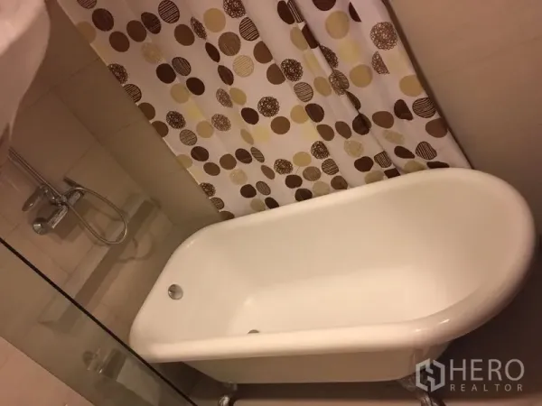 Condominium for rent in Khlong Toei, Bangkok - Bathroom with soaking bathtub, shower set, and a polka-dot patterned curtain.
