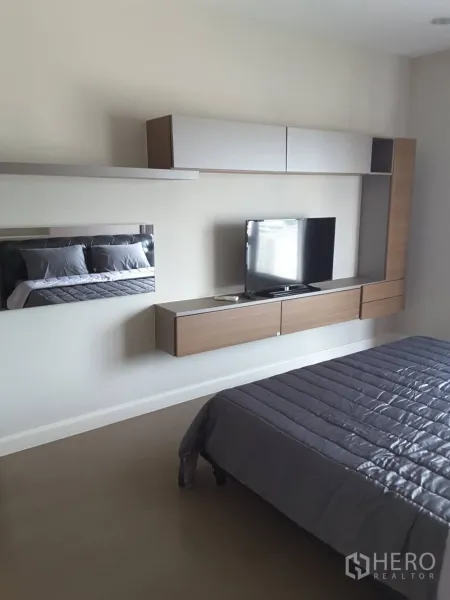 Condominium for rent in Khlong Toei, Bangkok - Master bedroom featuring a wall-mounted TV and floating storage cabinets with a gray duvet.