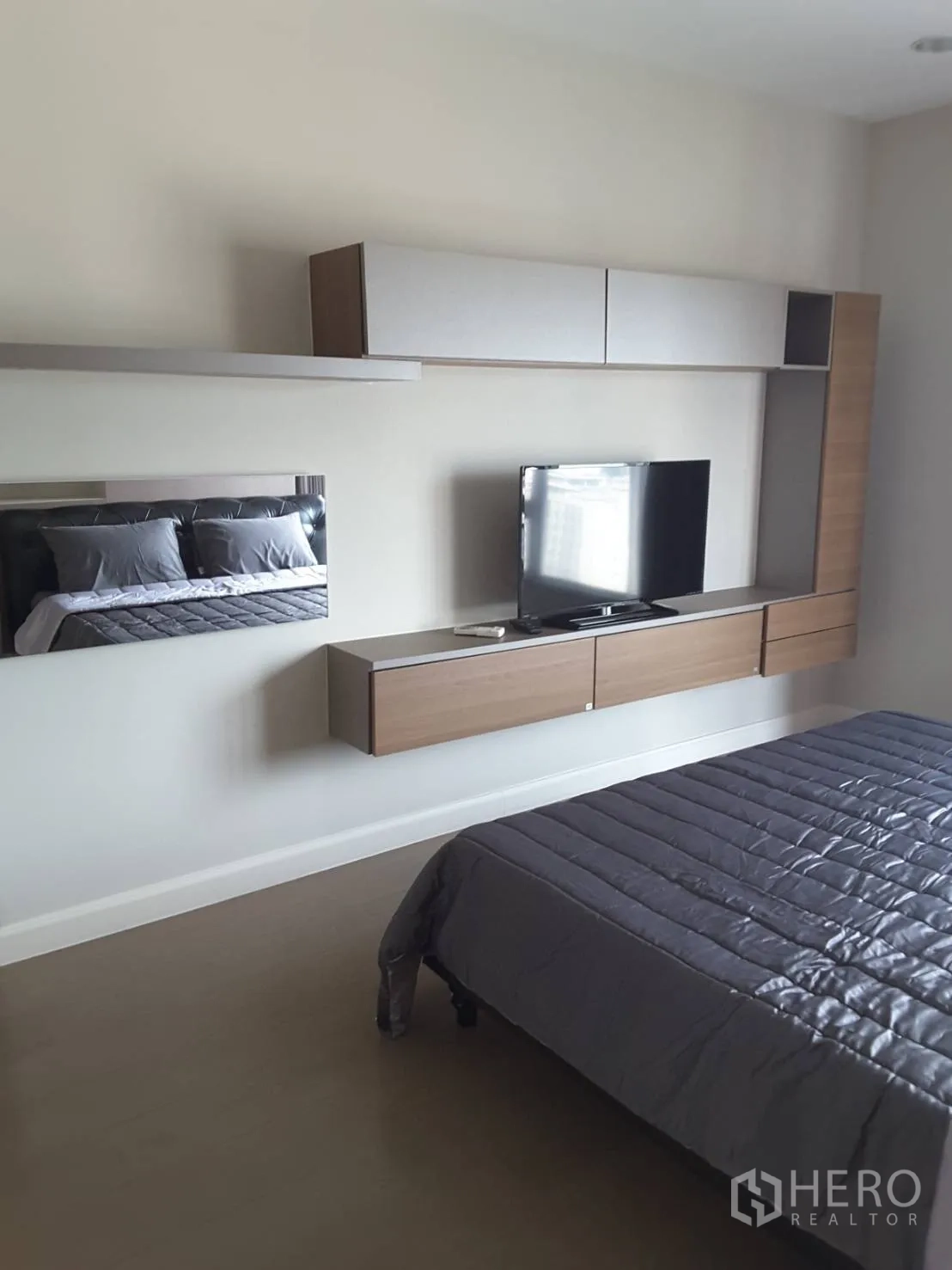 Condominium for rent in Khlong Toei, Bangkok - Master bedroom featuring a wall-mounted TV and floating storage cabinets with a gray duvet.