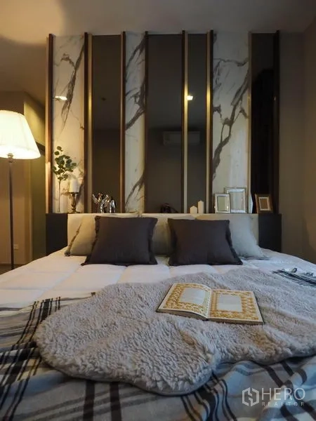 Condominium for rent in Khlong San, Bangkok - Bed close-up with throw and pillows in a softly lit bedroom with marble details.