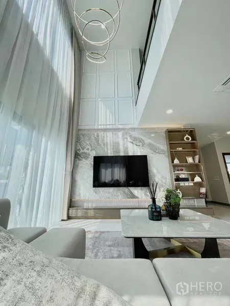 Detached House for rent in Bang Phli, Samut Prakan - Double-height living room featuring a marble TV wall, statement chandelier and tall curtains.