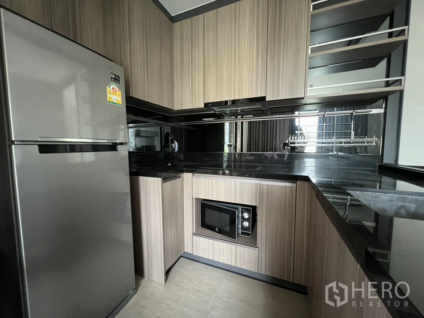 คอนโด for rent in Watthana, Bangkok - ครัวรูปตัวแอลทันสมัยพร้อมตู้เย็น ไมโครเวฟ และท็อปสีดำมันวาว