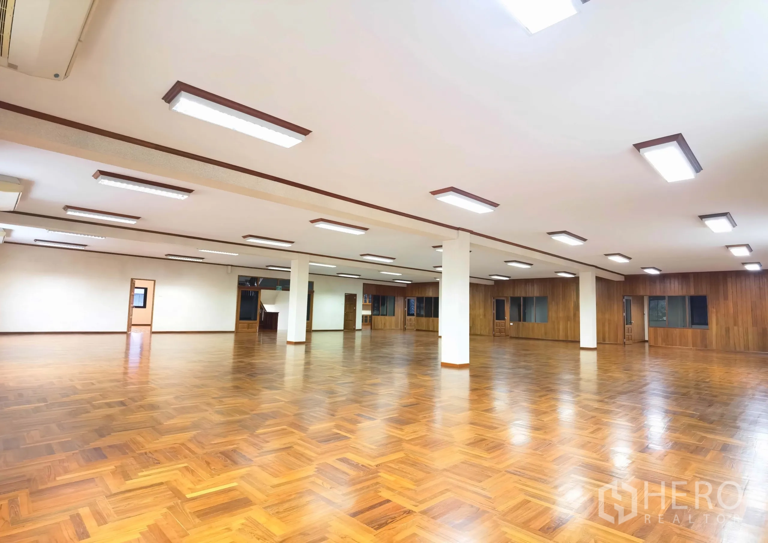Warehouse for rent in Samut Prakan - Expansive office hall with parquet wood flooring and ceiling lights inside the warehouse building.