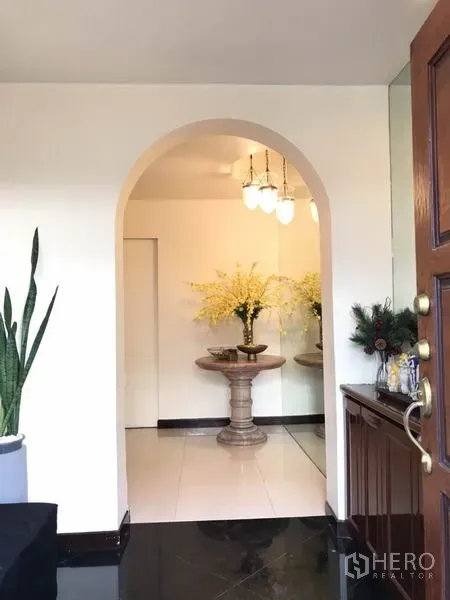 Detached House for rent in Phra Khanong, Bangkok - Arched entry foyer with a pedestal table, floral arrangement, and pendant lights.