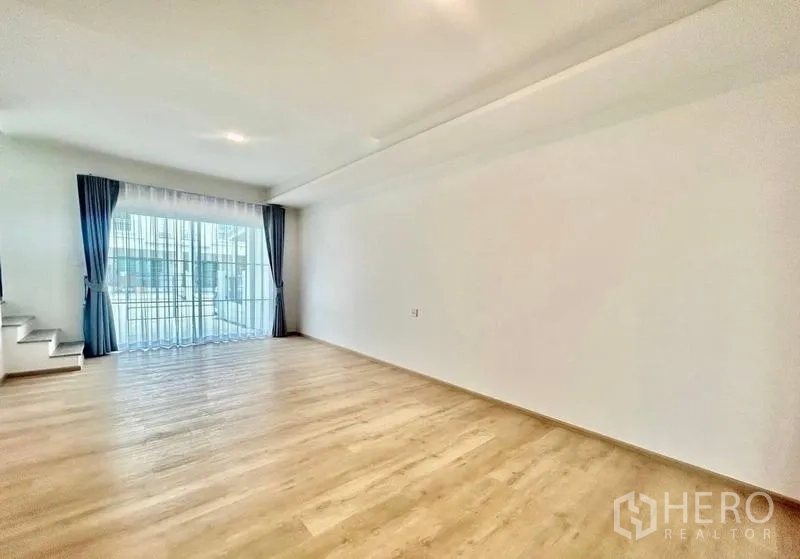 Townhouse for rent in Bang Phli, Samut Prakan - Spacious family room with large window, curtains and wood-look flooring.